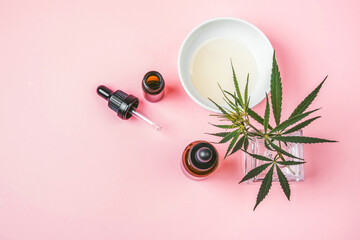 Cannabis leaf, hemp oil bottle and cup with oil on a pink background. 