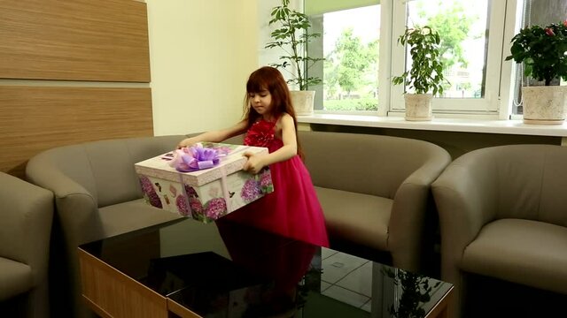 Cute excited little girl happy child kid in beautiful pink dress shaking huge present gift box wrapped in violet ribbon