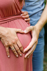 Mother and father hold hands on a pregnant belly. Husband hugs his pregnant wife in pink dress