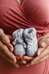 A man father holds the hands of a woman's mother in his arms against the background of a pregnant belly. Parents hold little booties in their hands