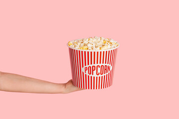 Millennial girl holding bucket of fresh crunchy popcorn over pink background, close up