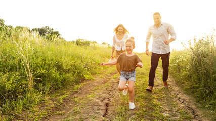 Happy parents and kid running together outdoor in summer