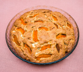 A large, round baked apple and apricot pie stands in a glass form on a table with a pink tablecloth. Delicious, fresh dessert.