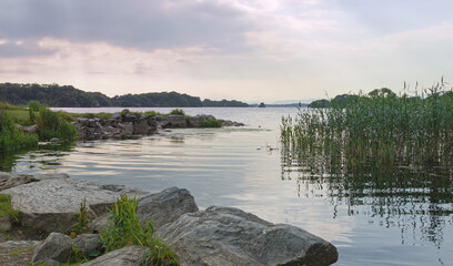 Rays of cool evening light fall on the tranquil waters of Lough Leane (Lower Lake), Killarney,...