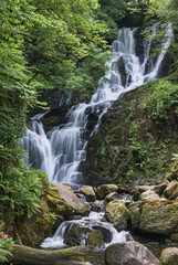 Fototapeta na wymiar Torc waterfall, Killarney, Co Kerry, cascades down the mountain side over moss covered rocks amid the trees and bushes of Ireland's native woodland. A long exposure emphasises the flow of the water.