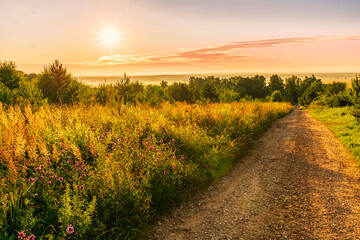 Fototapeta na wymiar Scenic view at beautiful sunrise in a far misty valley, bright crimson cloudy sky , trees and golden sun rays with glow, summer morning field landscape