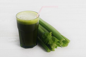 Fresh green celery juice in glass on white wooden background