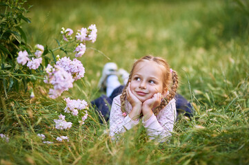 The little girl lies on the grass and holds her head with her hands. Girl makes different facial expressions