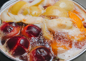 Fruit compote: apricots, plums, apples, cherries are cooked in a metal pan in boiled water with bubbles. Making juice on the stove.