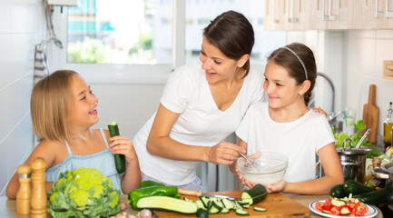 Portrait of single mother with two daughters cutting vegetables, preparing vegetarian dinner at home