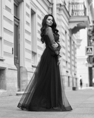 Elegant woman wearing long blue evening dress. Pretty lady posing outdoors. Fashionable stylish model. Fashion outdoor portrait. Female with long wavy hair standing at city street