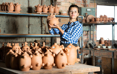Cheerful girl worker of pottery workshop showing finished ceramic production
