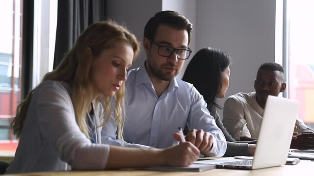 Helpful experienced male boss mentor teacher instructing young female intern trainee new worker making notes explaining new online project looking at laptop computer at apprentice course in office
