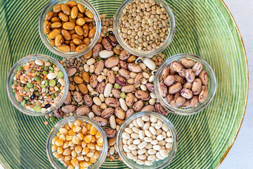 Pile of legumes including beans, peas, lentils arranged on a green plate.