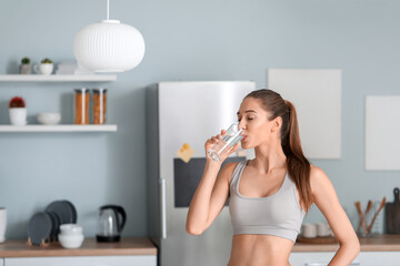 Beautiful young woman drinking water in kitchen