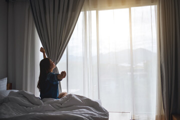 A young woman do stretching after waking up in the morning on a white cozy bed at home