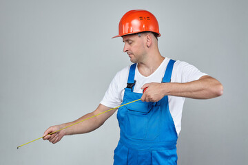 adult man in a construction helmet takes measurements with a tape measure. photo session on a white...