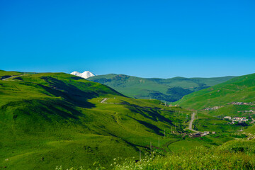 Fototapeta na wymiar Elbrus and Green Meadow Hills at a Summer Day. North Caucasus, Russia