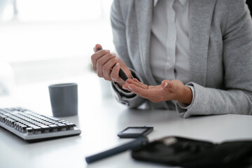 Close up of businesswoman using lancet pen in office. Young woman checking blood sugar level	