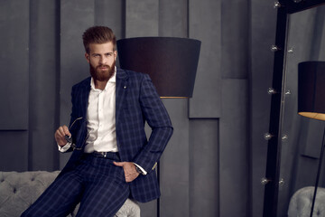 Handsome stylish man in blue suit in a cage at home siting on sofa.