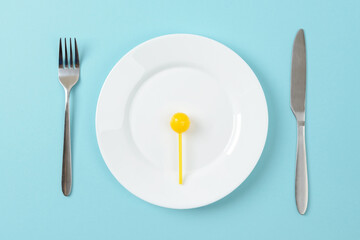 Yellow sweet caramel candy on a white dinner plate, table knife and fork on a blue background. Concept of unhealthy eating with excess carbohydrates.