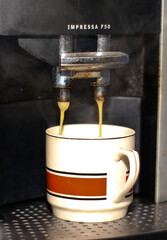 A cup is filling with hot coffee from the coffee maker machine.