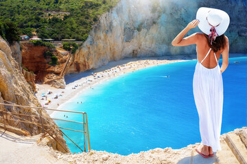 Eine Frau mit weißem Sommer Hut gemießt die Aussicht auf den Strand von Port Katsiki mit türkisblauem Meer und steilen Felsklippen, Lefkada, Griechenland