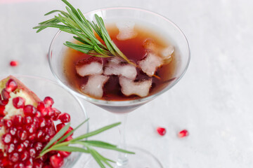 Cold non-alcoholic pomegranate cocktail with rosemary on a light pink background. Natural healthy drink