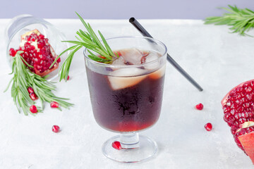 Cold pomegranate non-alcoholic cocktail with rosemary on a light background. Fruit grains in a glass. Natural healthy drink