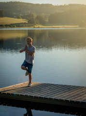 Fototapeta na wymiar young man on wooden pontoon or pier practicing yoga & relaxing with reflection in water .on holiday
