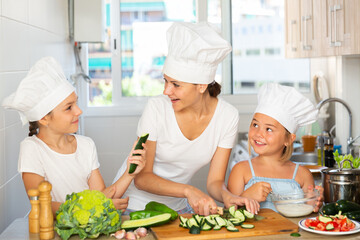 Little cooks learn with their mom how to cook a vegetable salad in the kitchen