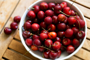 Cherries on wooden table with white porcelain bowl.