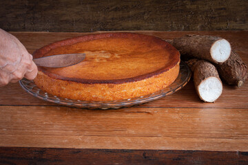 Hand cutting manioc cake on wooden background.