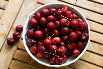 Cherries on wooden table with white porcelain bowl.