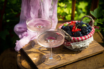 Outdoor summer lifestyle with a gourmet picnic laid out on a chair in a garden with berries, pie and pink drink in stylish glasses