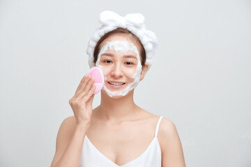 Happy young Asian woman applying foaming cleanser on her face and wearing towel on her head.