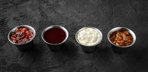 Obraz na płótnie Canvas Set of different sauces, mayonnaise, hot pepper, tomato garlic sauce, berry spicy sauce in bowl on black stone background