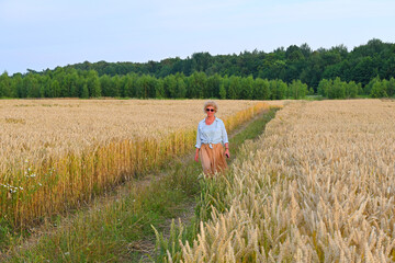 A beautiful, slender woman among a wheat field in the rays of sunrise. A slight smile can be seen on her face. The photo looks like a painting.