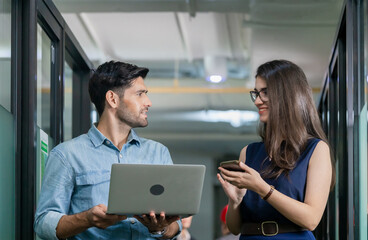 Young businessman holding laptop and walking discusses work with female team, business team of coworkers meeting in creative office
