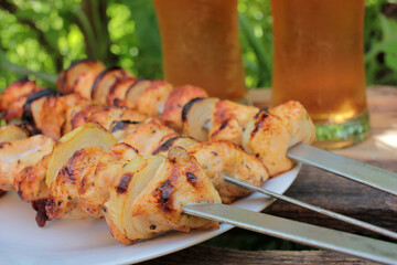Chicken kebab on skewers and beer in glasses. Backyard bbq summer outdoor party. Natural green blurred background. Selective focus