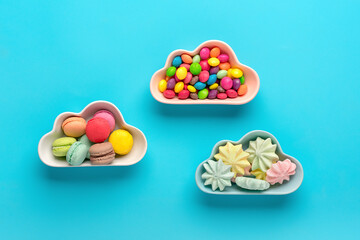 sweets - lollipop, meringues, macaroon in bowl in shape of cloud, chocolate, with colorful topping donut isolated on blue background Flat lay Top View Knolling Unhealthy and tasty food concept