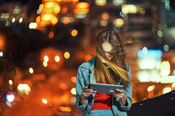 Girl on night cityscape background with street lights, using a digital tablet