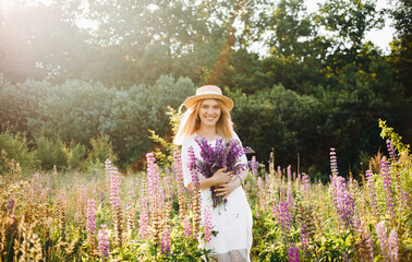 Gentle girl in a white dress and hat posing in a field with a bouquet in her hands.