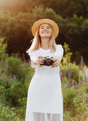 Beautiful blonde woman with a camera in her hands posing in a lupine field.