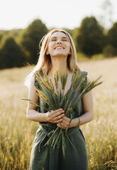 Attractive girl with short blond hair posing in a wheat field holding spikelets in her hands....