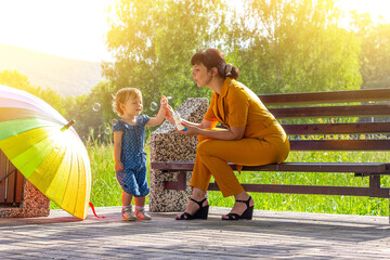 a young beautiful mother with a small daughter sit happy on a bench in the Park and blow soap...