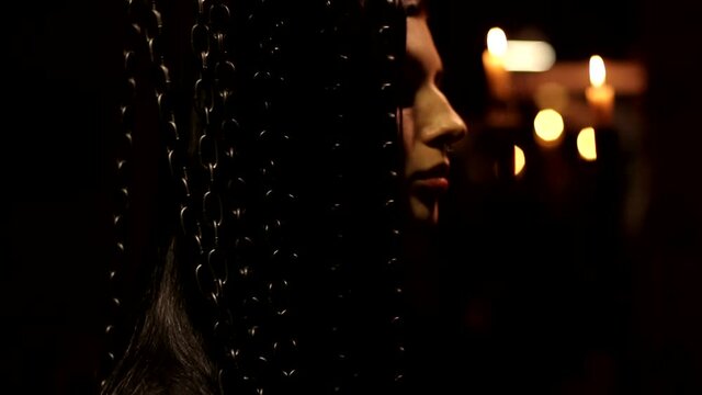 Warm candle light black mysterious background shot of dark hair beautiful young woman standing behind the chain curtain