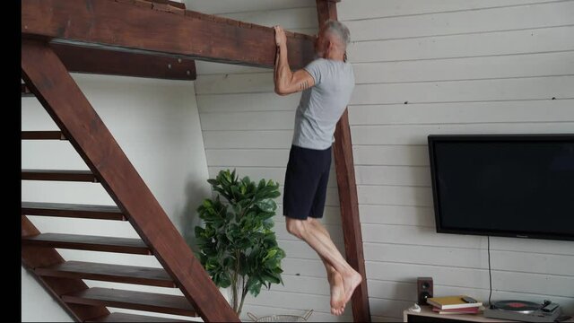 Training at home. Athletic and strong mature man doing pull ups exercises on wooden horizontal bar at home