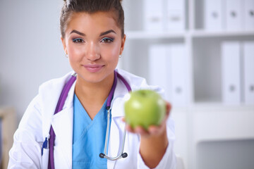 Female doctor hand holding a green apple, sitting at the desk