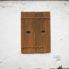 Carved wooden shutters on a white brick wall.